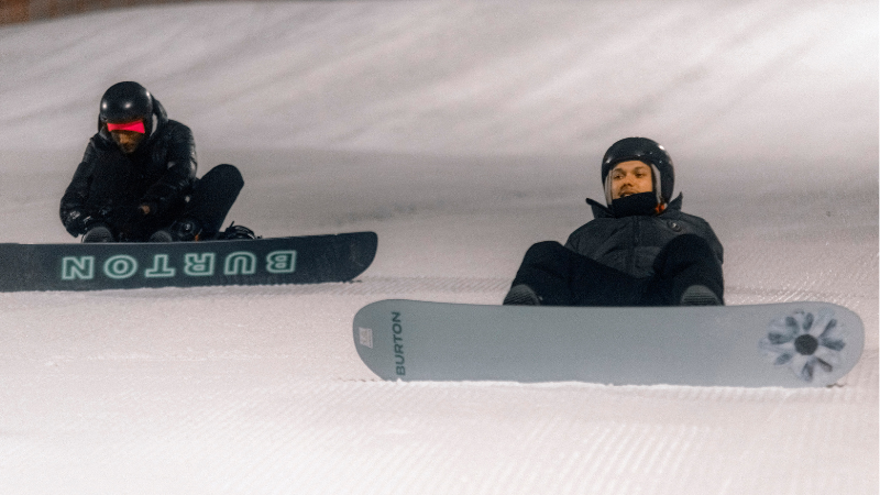Två killar med snowboard som sitter i backen.